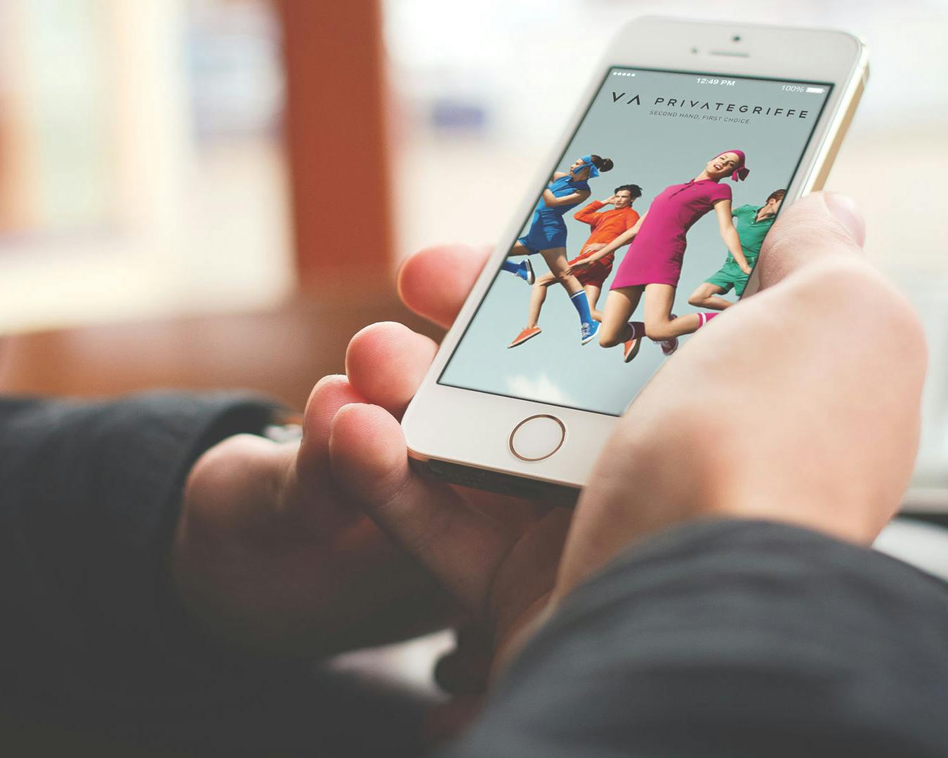 Una persona tiene un iPhone en la mano que muestra la pantalla de una aplicación de moda con varias personas modelando atuendos coloridos.