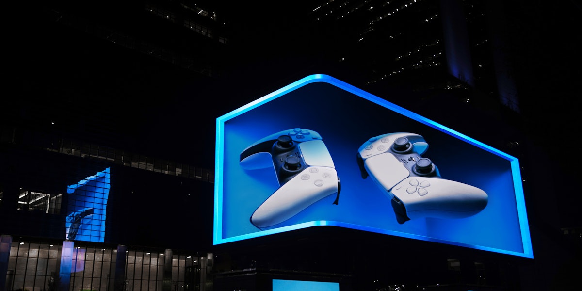 A monumental anamorphic 3D billboard at night showing the PlayStation 5 console and DualSense controller in electric blue.