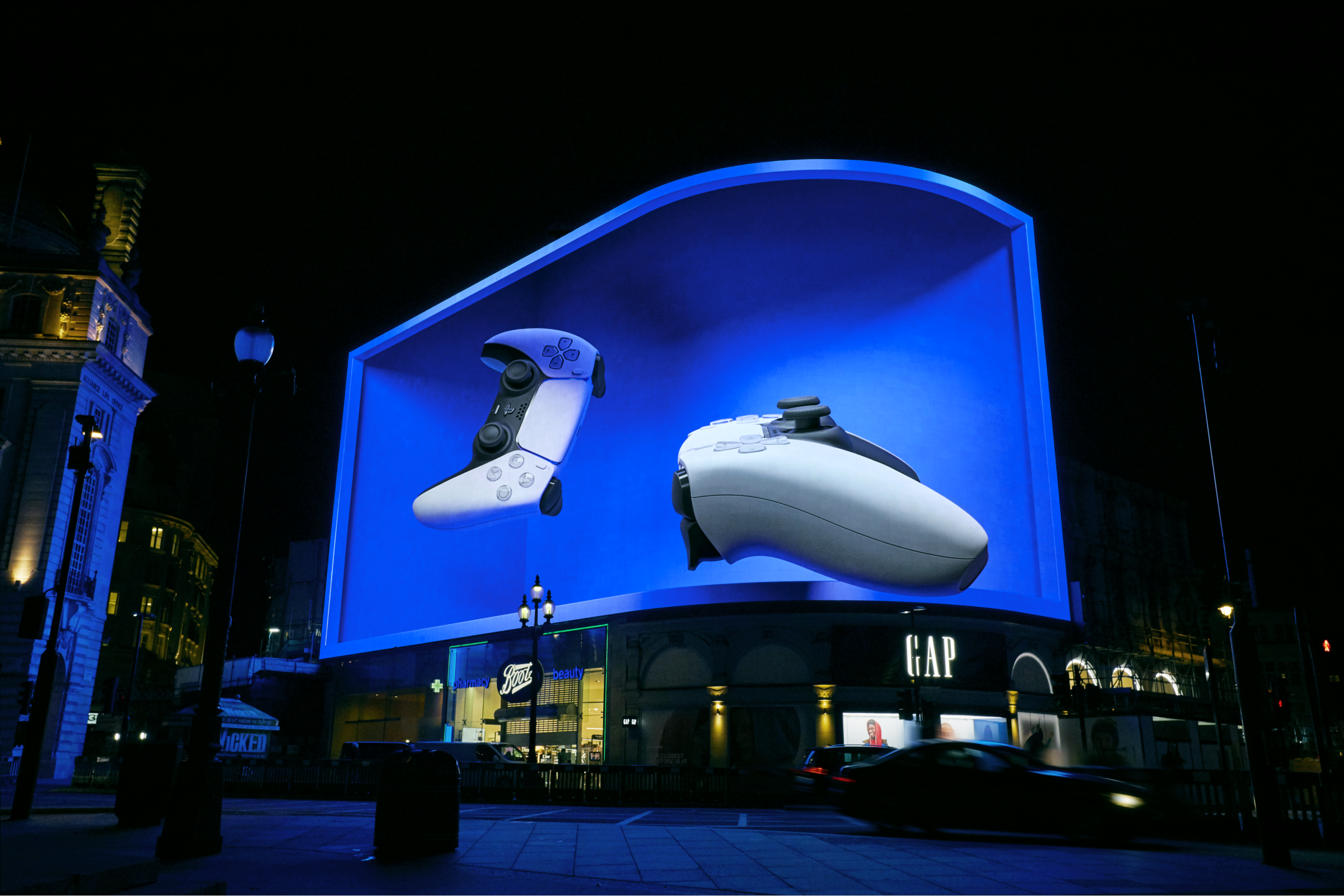 The PlayStation 5 launch takeover at Piccadilly Circus, London: a giant curved 3D billboard showing a DualSense controller glowing over the night-time square.