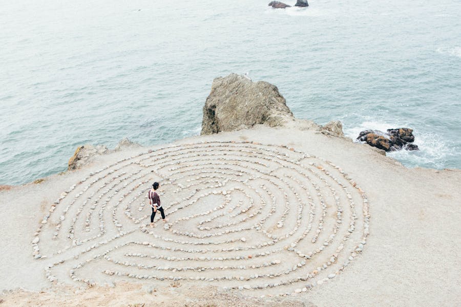 Una persona cammina su una spiagga in cui è disegnato un labirinto concentrico con le pietre.