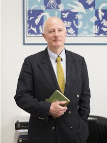 Foto del Professor Stefano Pallanti in giacca e cravatta, in piedi davanti a un tavolo, con in mano un libro