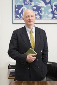 Foto del Professor Stefano Pallanti in giacca e cravatta, in piedi davanti a un tavolo, con in mano un libro