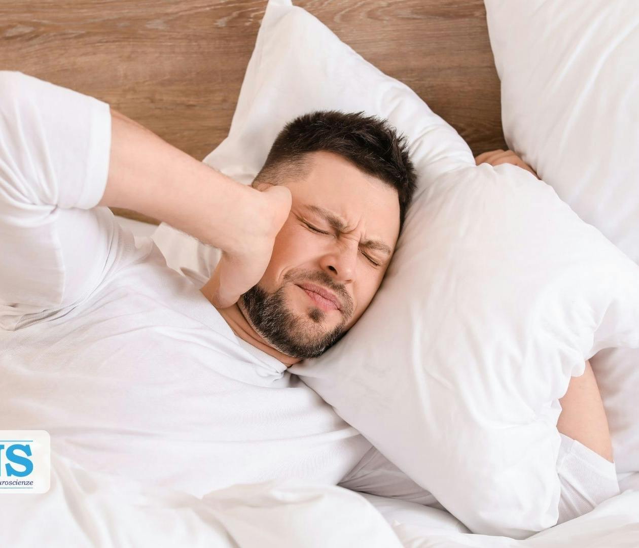 Una persona a letto si copre un orecchio infastidita dal tinnito.