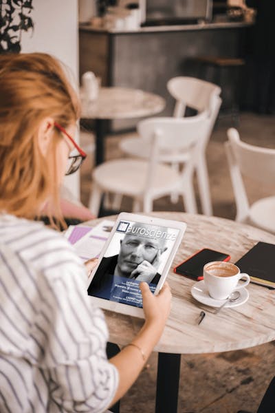 Woman sitting at a café table reading Firenze Neuroscienze Magazine on her tablet.