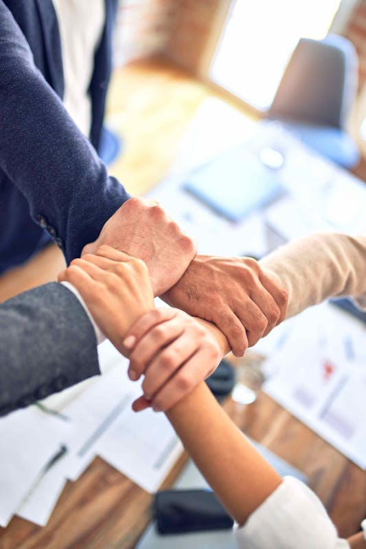 Picture of four hands of four different people holding each other's wrists to form a square.