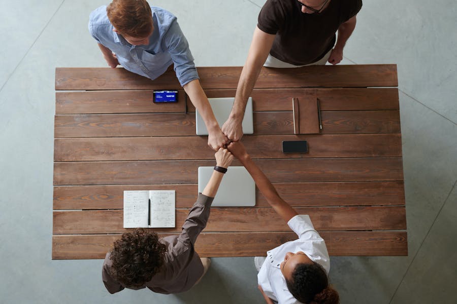 Four people sitting at a table touching each other with their fists as a sign of alliance and cooperation.