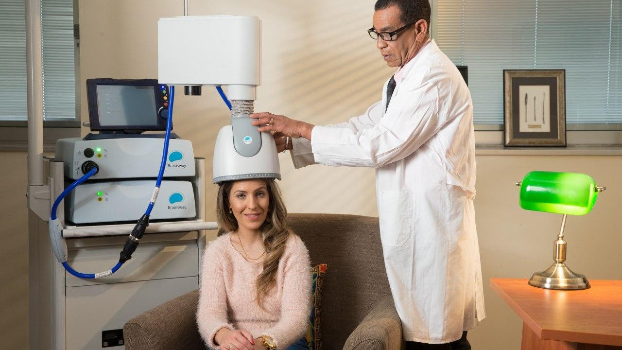 Smiling woman sitting in a chair during a Deep TMS session conducted by a physician.