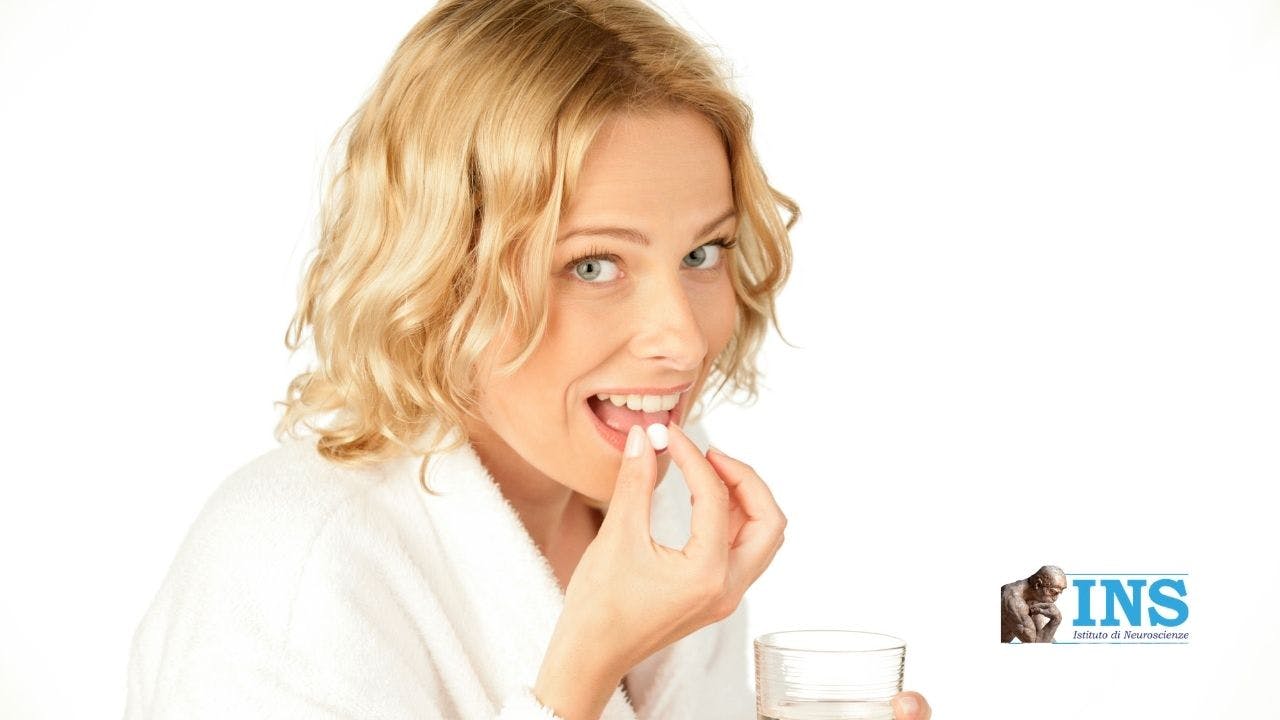 Smiling blonde woman carrying a pill to her mouth.