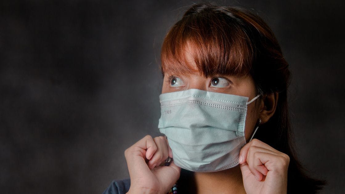 Girl placing a surgical mask on her face.