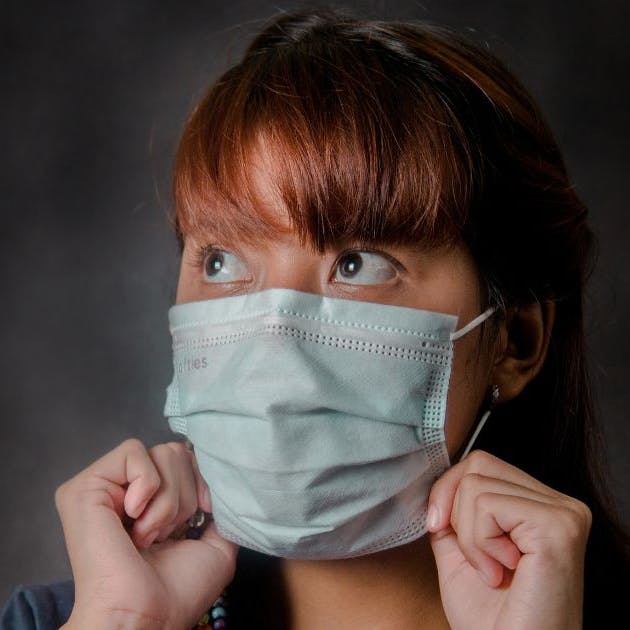 Girl placing a surgical mask on her face.