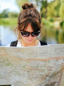 Persona con gli occhiali da sole guarda una mappa per orientarsi con alle spalle un lago