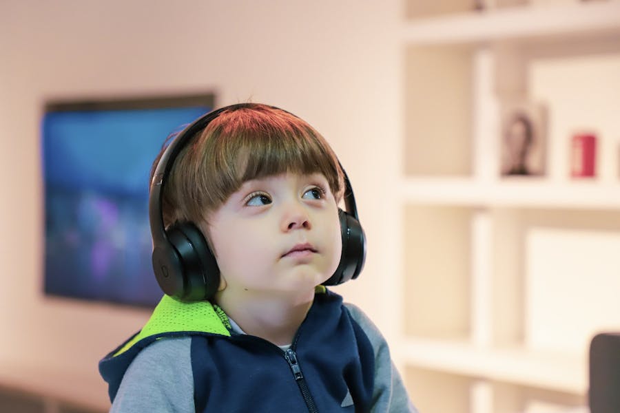 Autistic child with headphones over his ears next to a wooden bookcase.