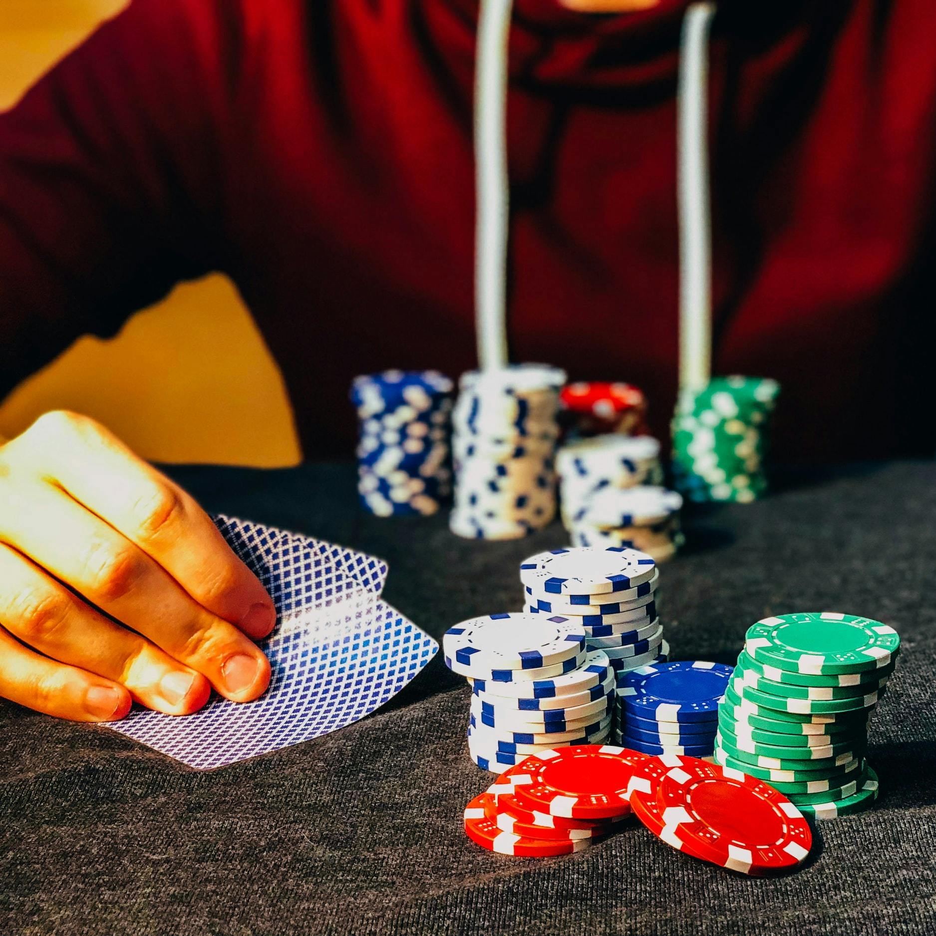 Persona che siede al tavolo con delle carte da gioco in mano e ha di fronte delle chip da poker