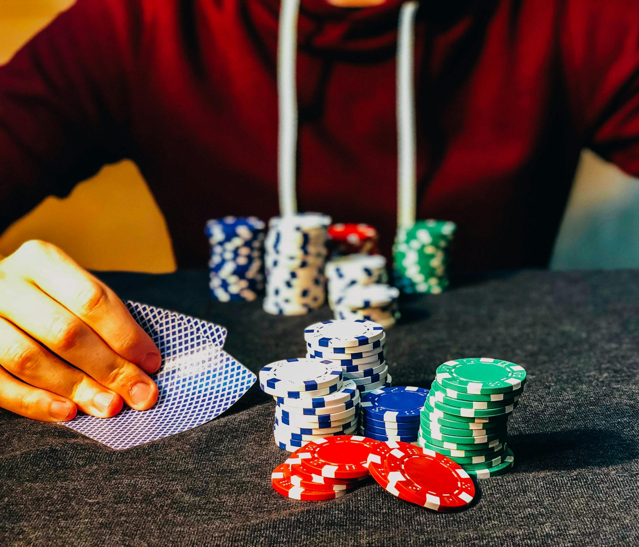 Persona che siede al tavolo con delle carte da gioco in mano e ha di fronte delle chip da poker