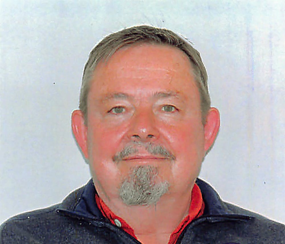 Foto di uomo sorridente con capelli, baffi e pizzetto brizzolati su sfondo bianco.