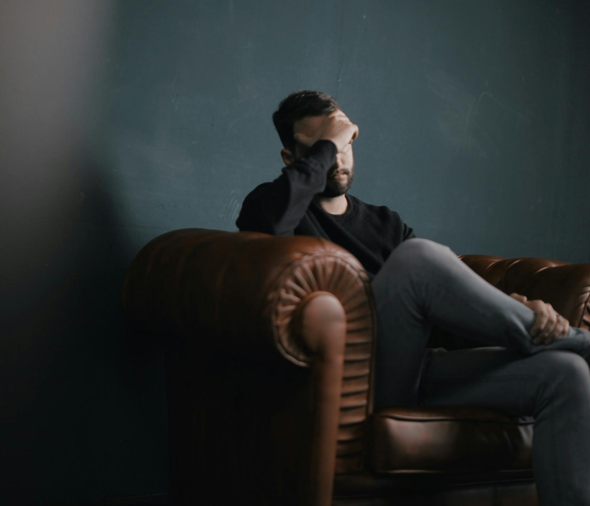 a man holds his head while sitting on a sofa