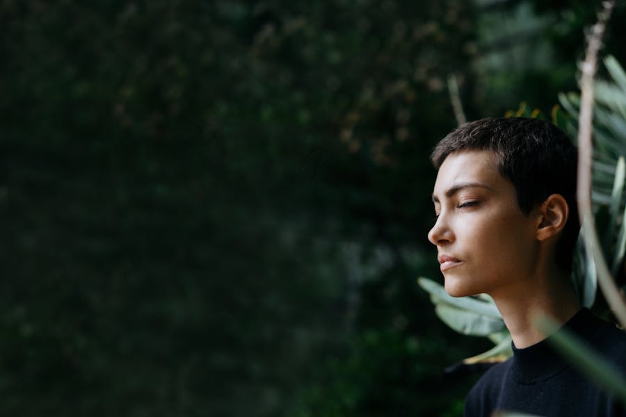 Thoughtful woman with closed eyes immersed in the greenery of a forest.