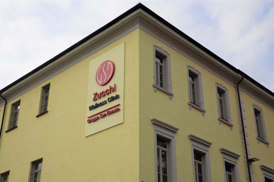 Front creamy yellow wall of the Zucchi Wellness Clinic, with a poster board that displays "Zucchi Wellness Clinic - Gruppo San Donato"