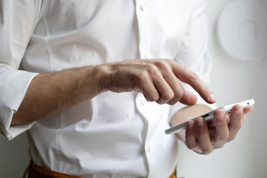 Man in white shirt touching the screen of a phone held in his left hand with the index finger of his right hand.