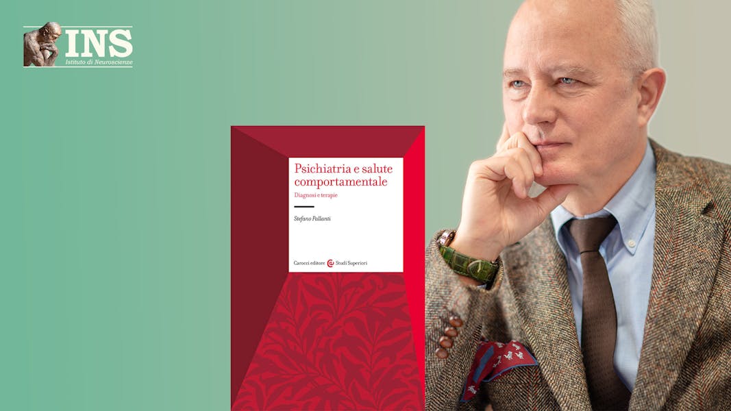 Stefano Pallanti in giacca, camicia e cravatta con il volto poggiato sulla mano destra in posa di osservazione e ascolto. Alla sua sinistra si trova la copertina rossa del suo libro "Psichiatria e salute comportamentale - Diagnosi e Terapie"