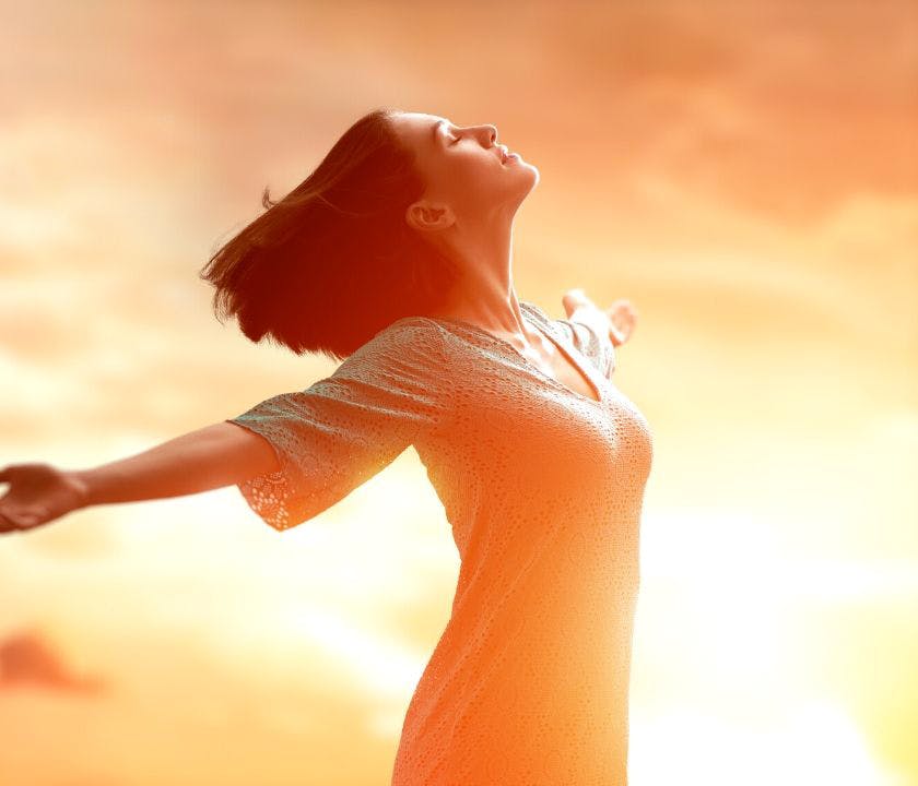 Picture of a woman enjoying the sun with open arms, standing in a field.