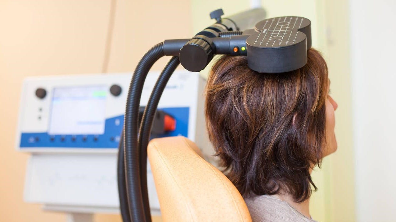 Donna seduta su una poltrona arancione con una bobina magnetica utilizzata per la Stimolazione Magnetica Transcranica appoggiata sulla testa.
