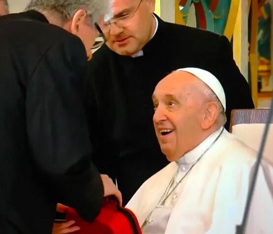 Papa Francesco seduto su una sedia mentre riceve da Adam Mester in regalo un dispositivo per la Foto-Bio-Modulazione contenuto all'interno di una custodia rossa.