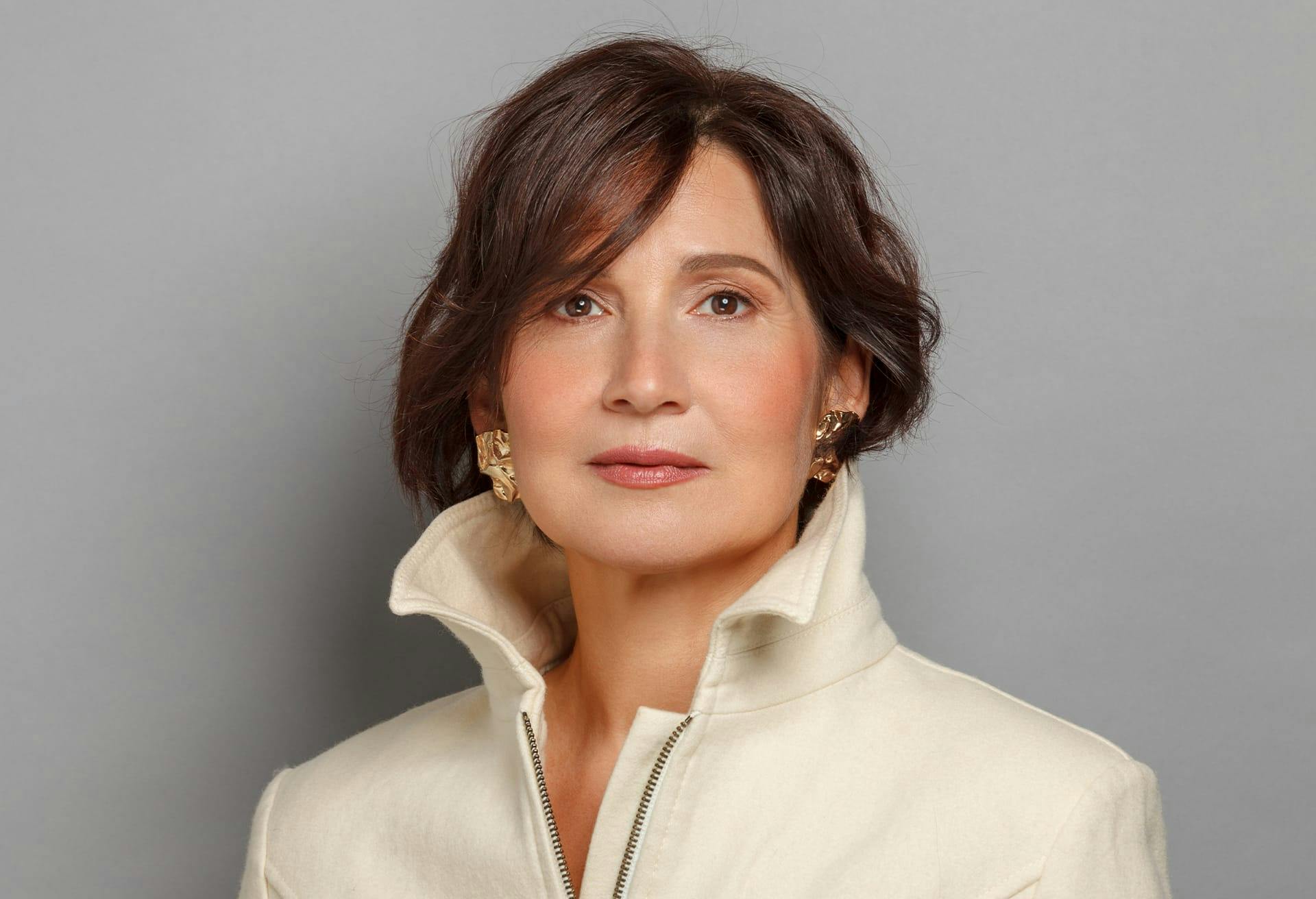 woman in a white jacket and gold earrings posing for a picture