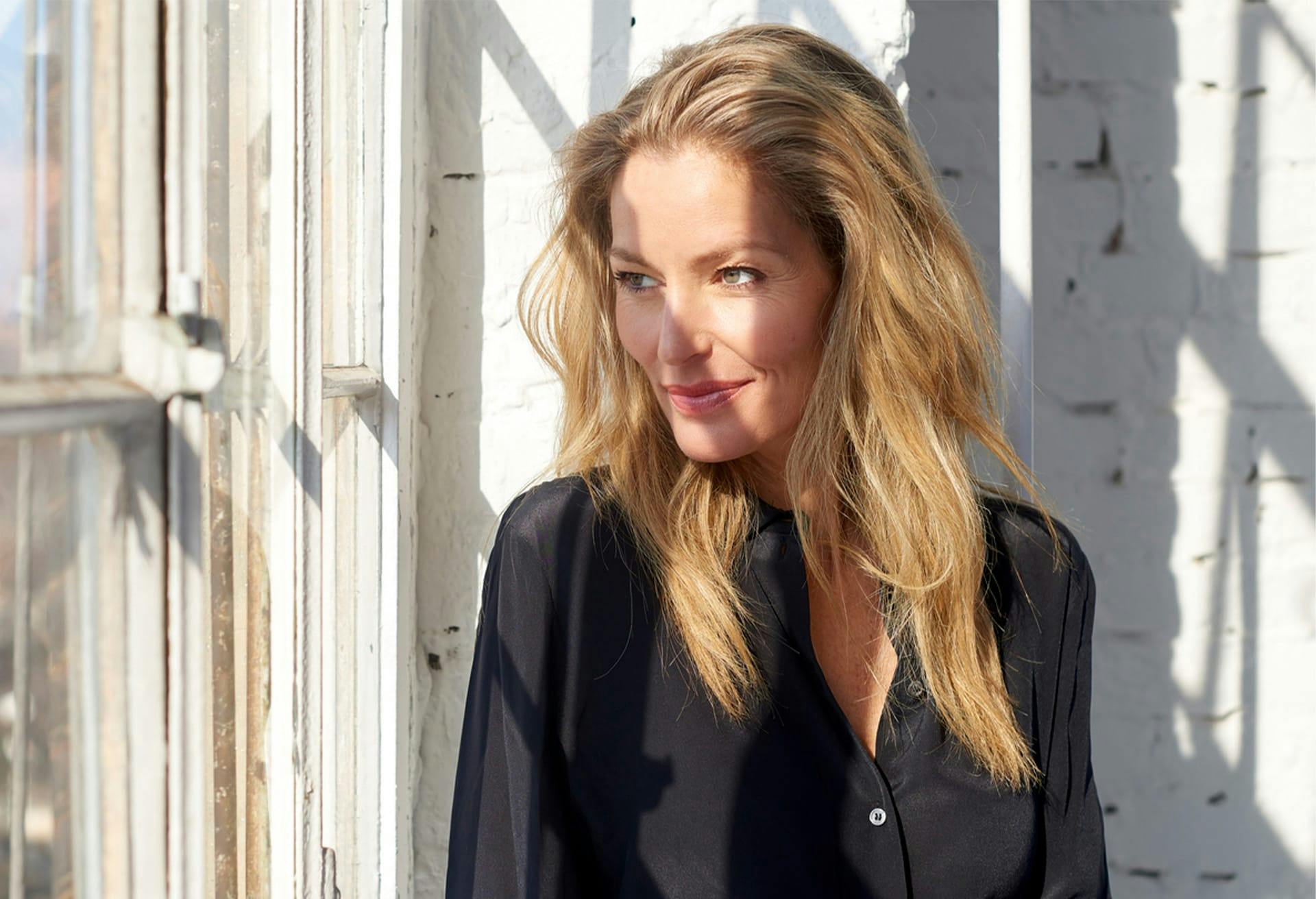blond woman with long hair standing in front of a window