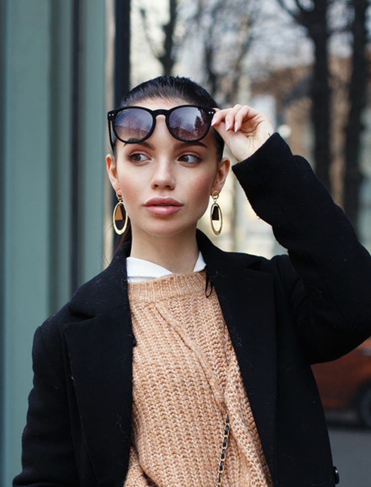 woman in a black jacket and sunglasses standing on a sidewalk