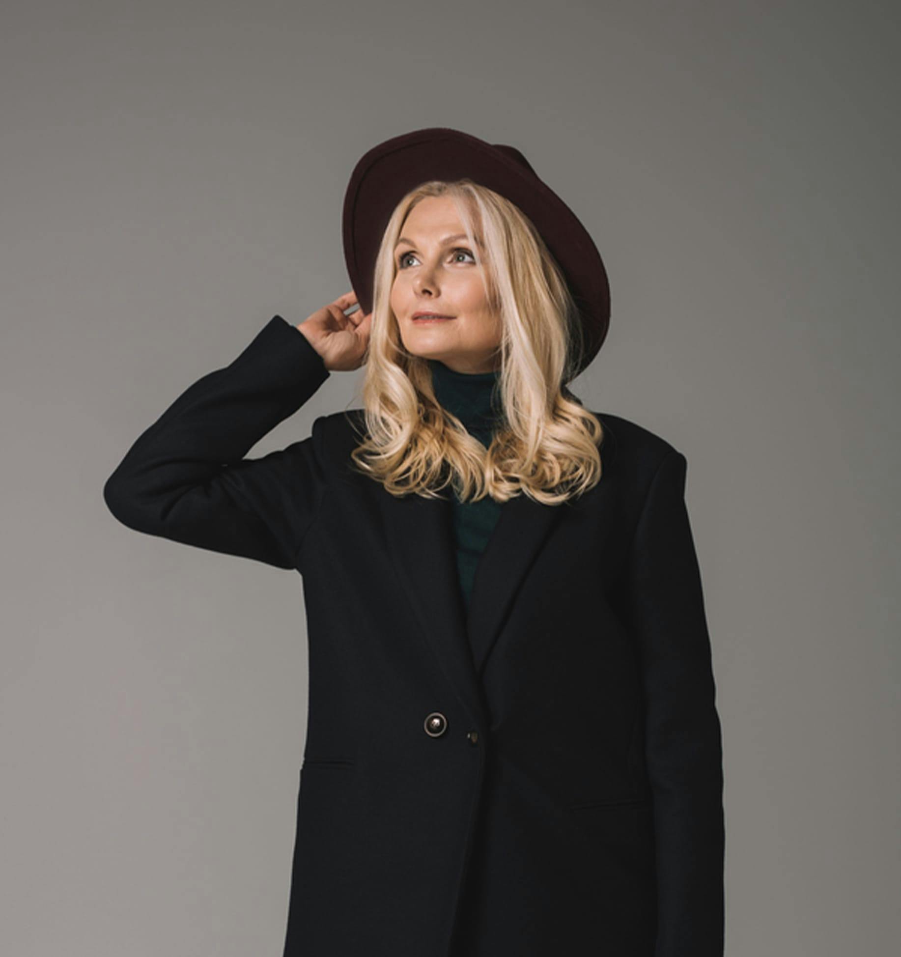 blond woman in black coat and hat posing for a picture