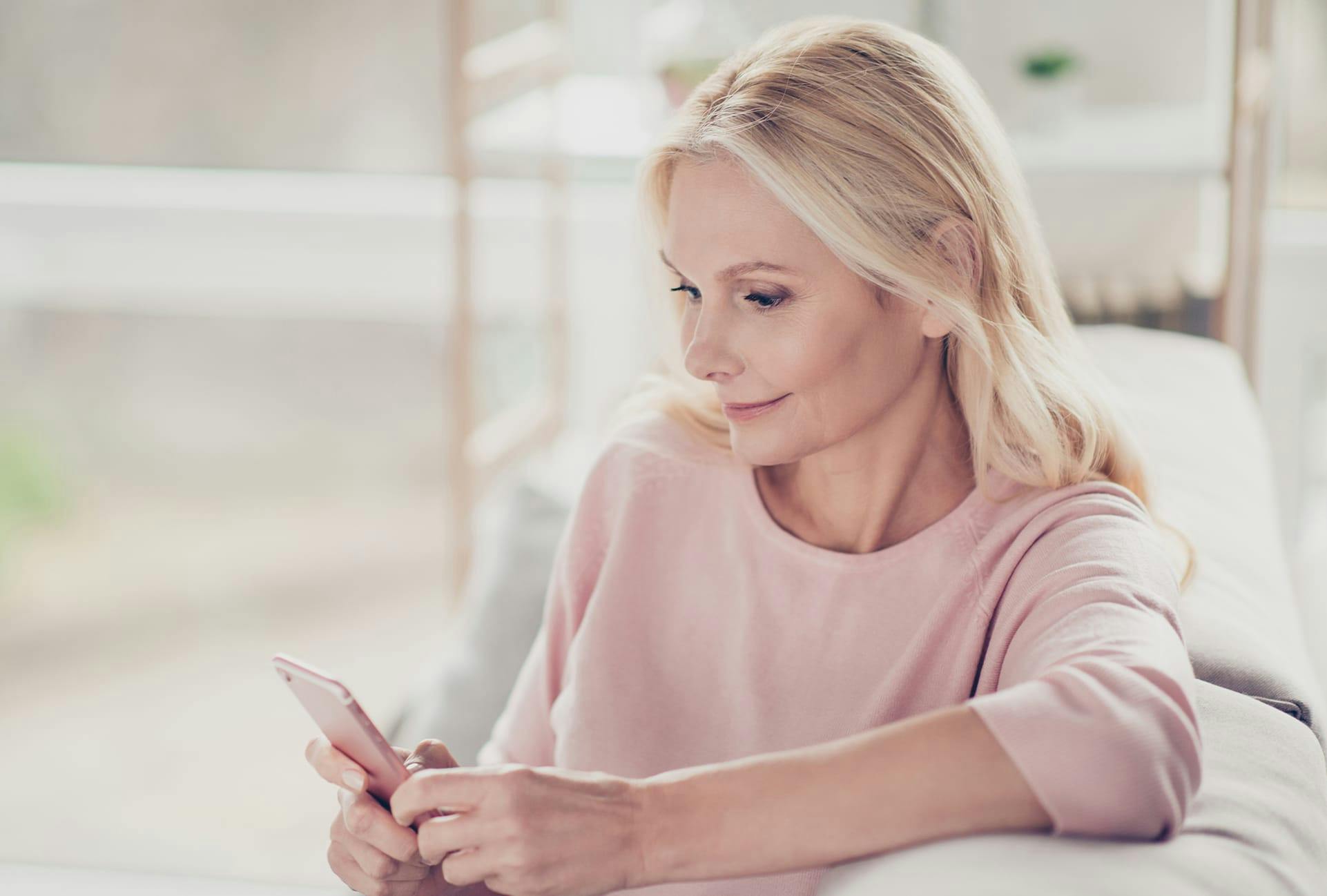 Woman with blonde hair wearing a pink shirt on her phone