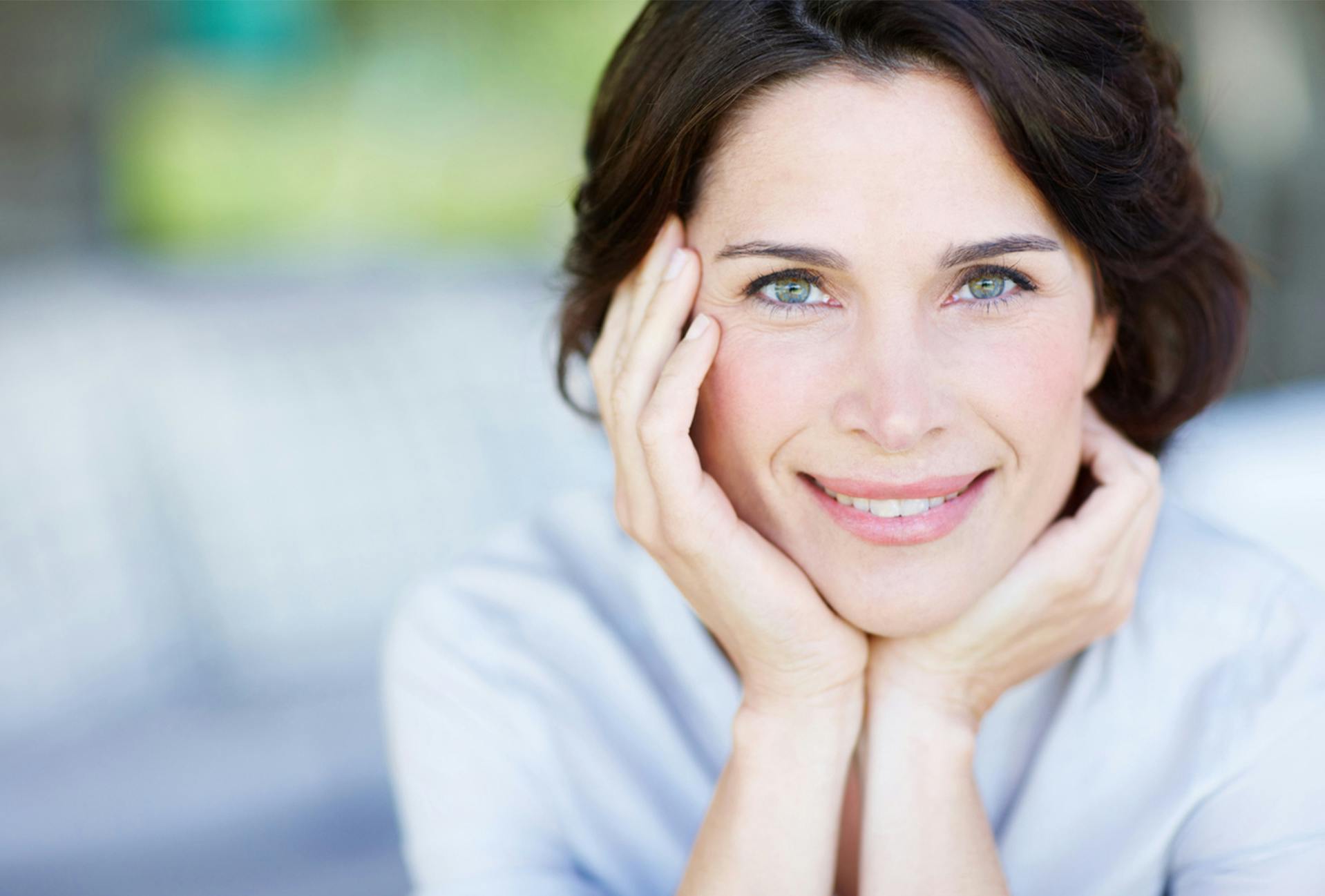 Woman with dark har smiling while resting her face on her hands
