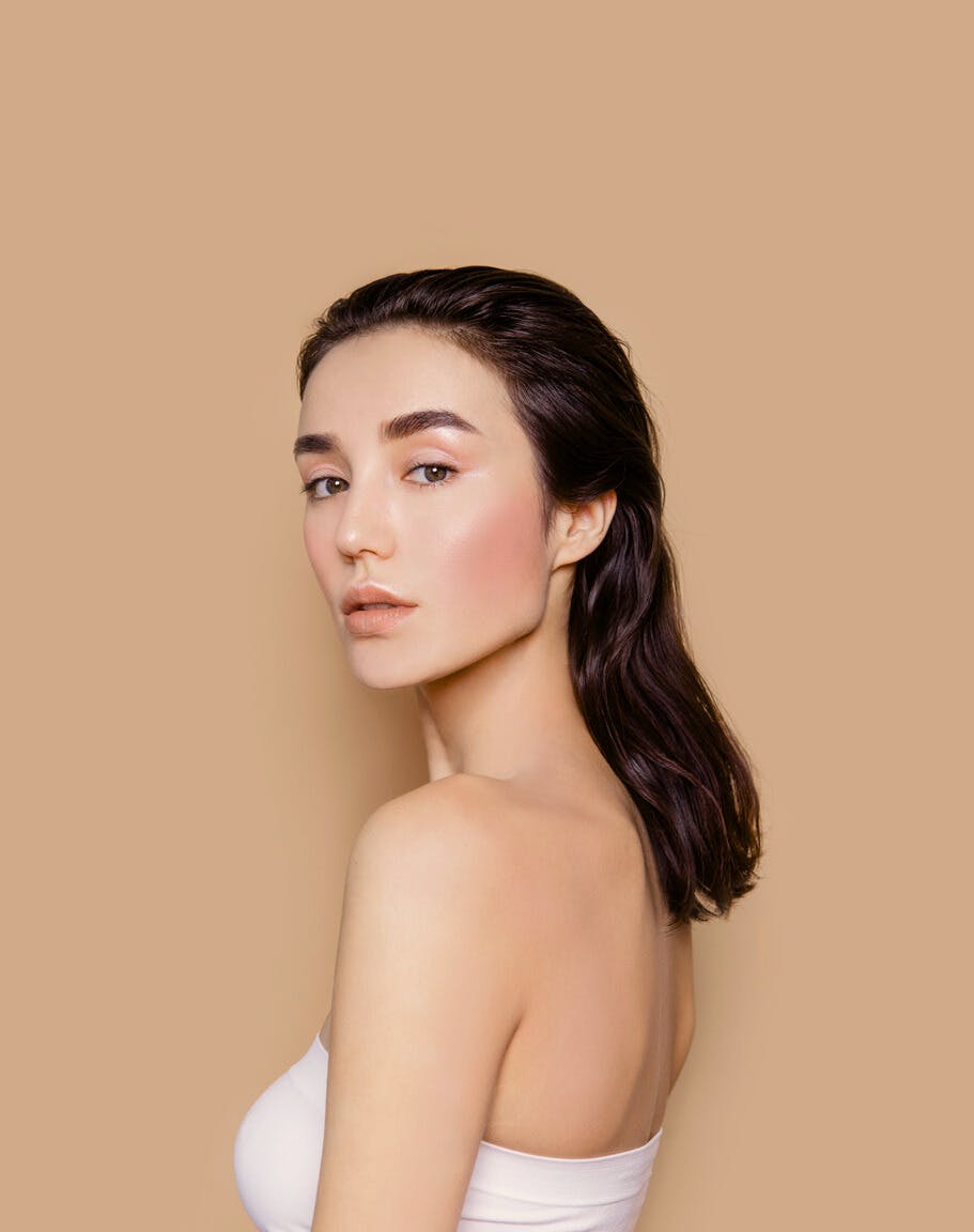Woman with gorgeous healthy skin shows the potential results of having AVAVA Treatments in a studio shoot with a white crop top on to showcase her face
