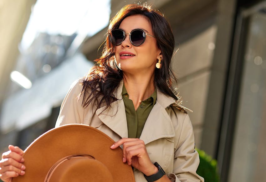 Woman in Beige Coat and Sunglasses Holding her Hat