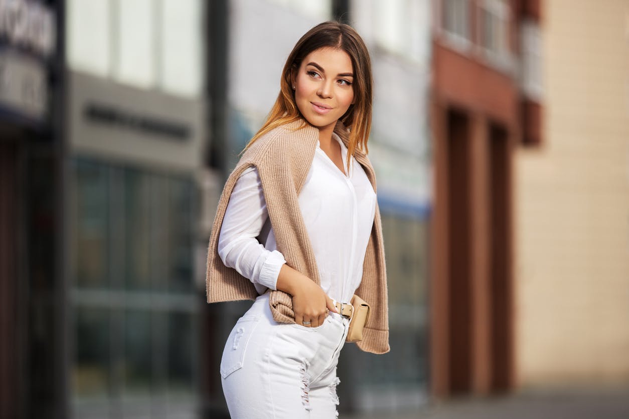 Woman wearing a white outfit with a tan sweater
