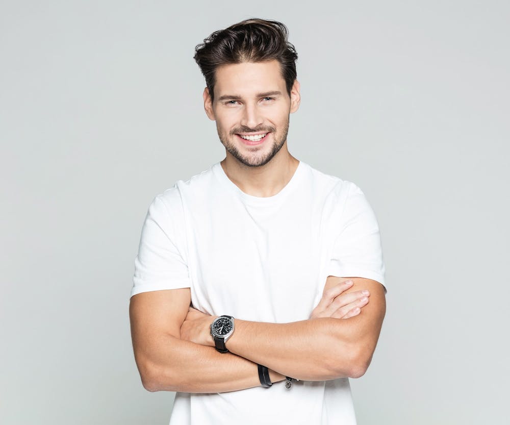 man in white shirt crossing his arms smiling