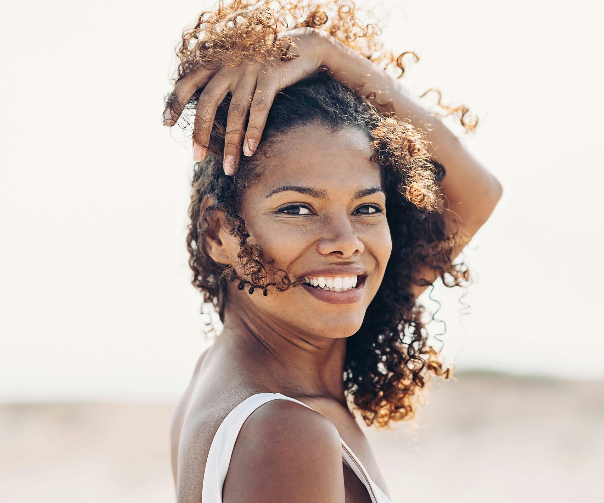 woman with curly hair keeping it off her face looking over her shoulder