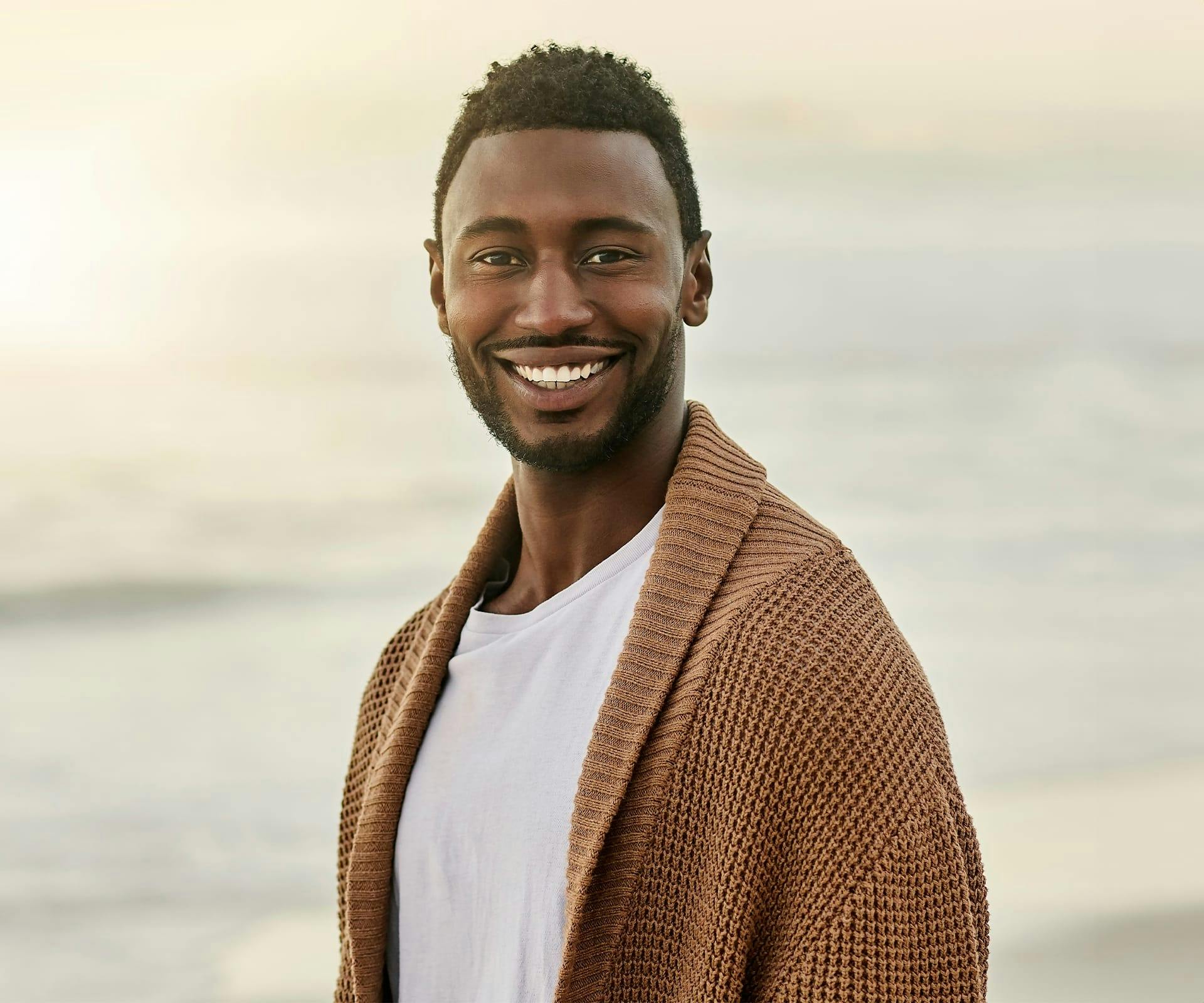 man with brown cardigan with water behind him