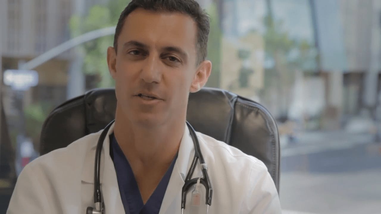 Dr. Tirgari sitting in an office chair explaining abdominal liposuction