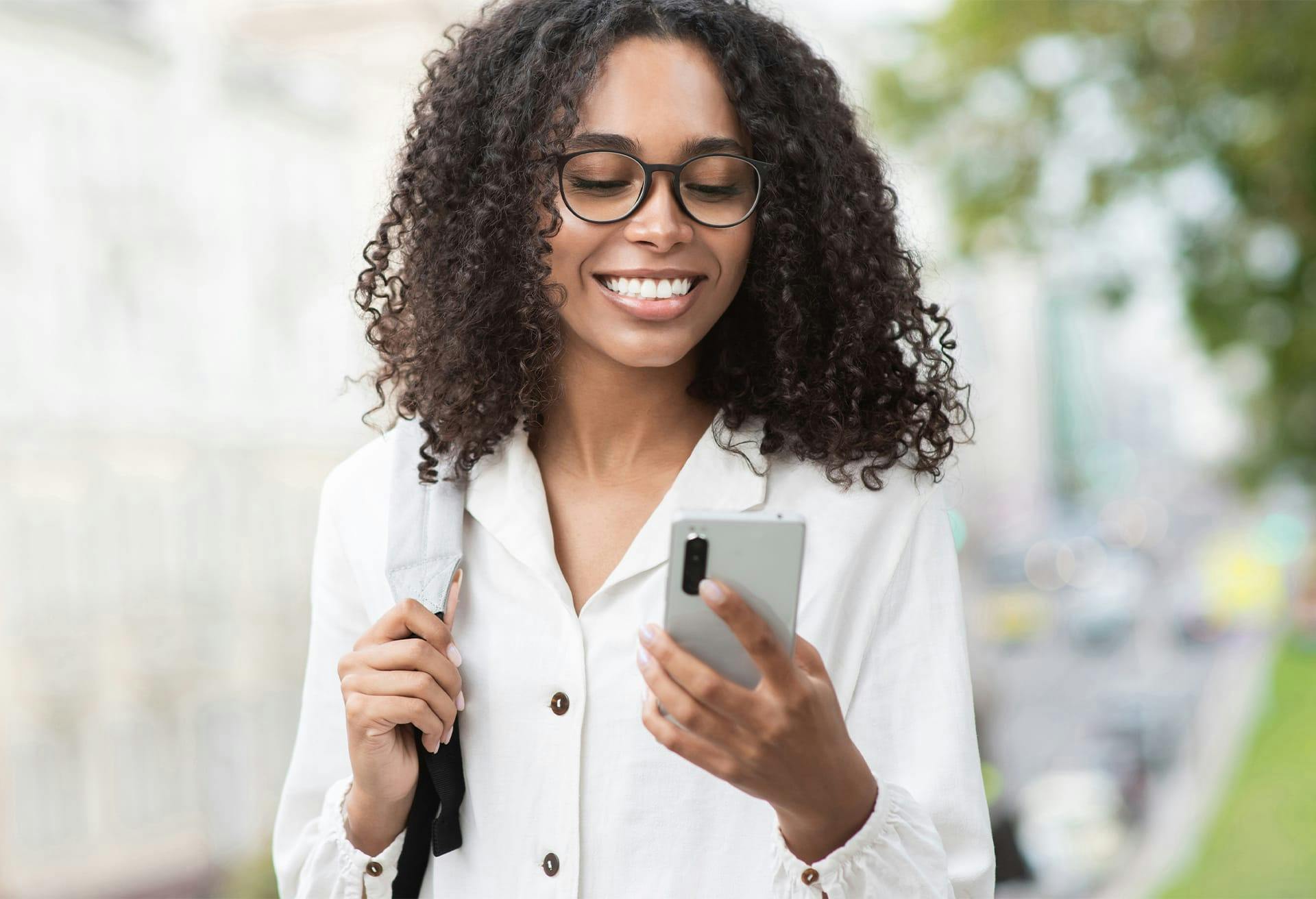 African American woman in white shirt smiling at her phone