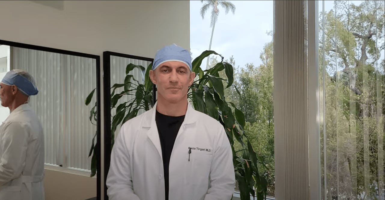 Dr. Tirgari explaining arm lipo while wearing a blue scrub cap