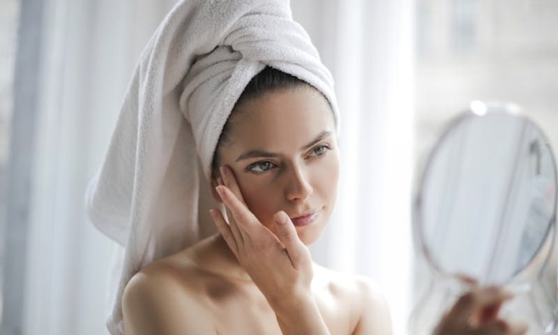 woman with towel on head looking at herself in mirror