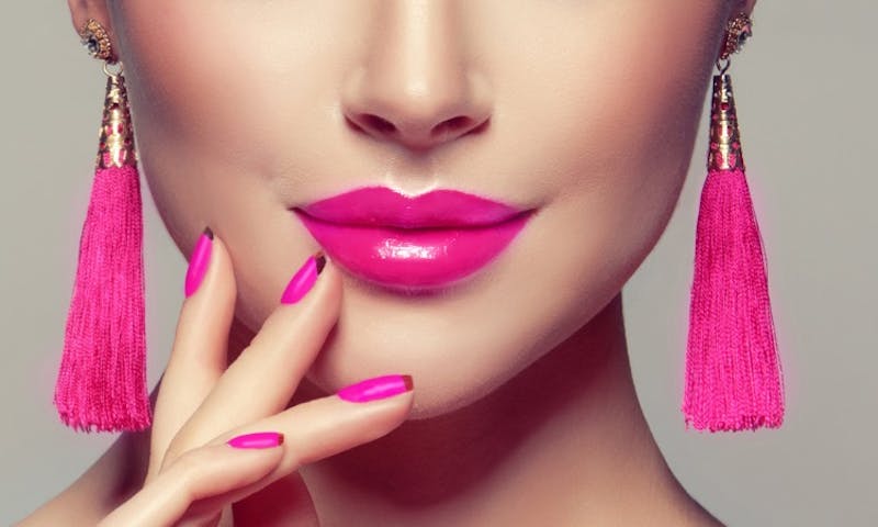 a close up of a woman with bright pink lipstick and tassel earrings
