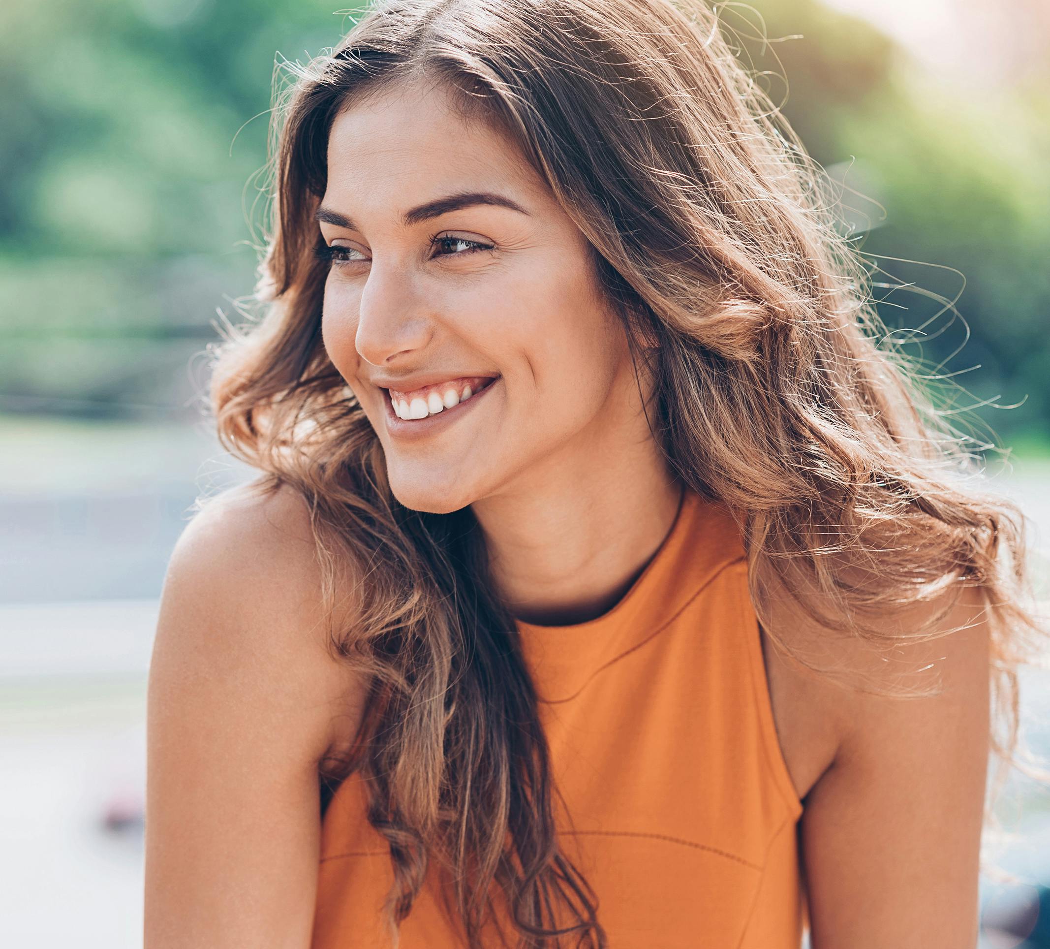 smiling woman with long brown hair and orange top looking at camera