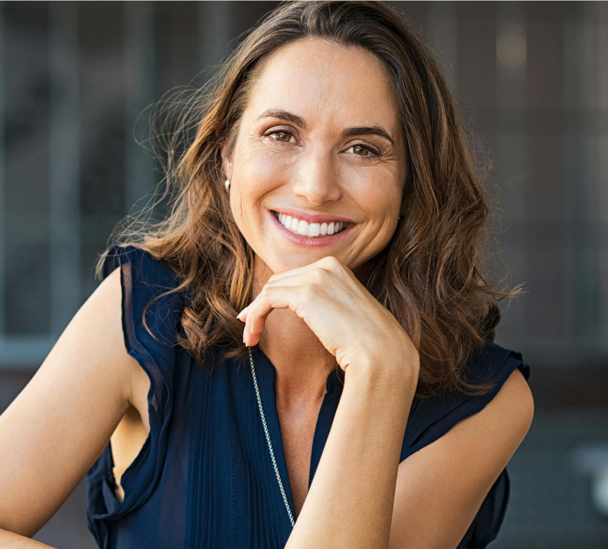 smiling woman with hand on chin, wearing blue dress and necklace