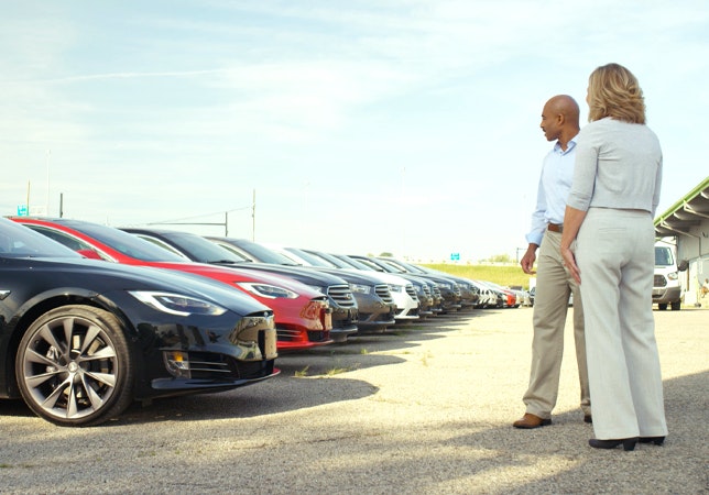 Man and woman standing in car lot evaluating cars