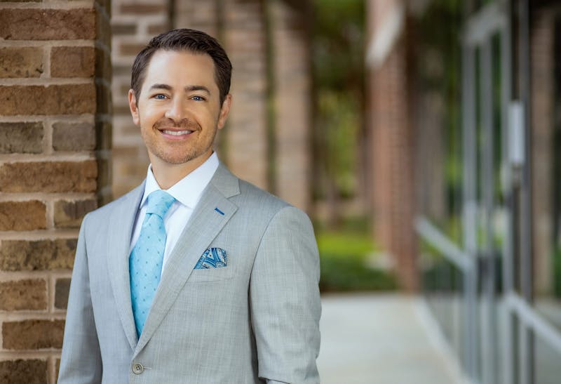 Dr. Robb standing outside of his practice in a grey suit and blue tie