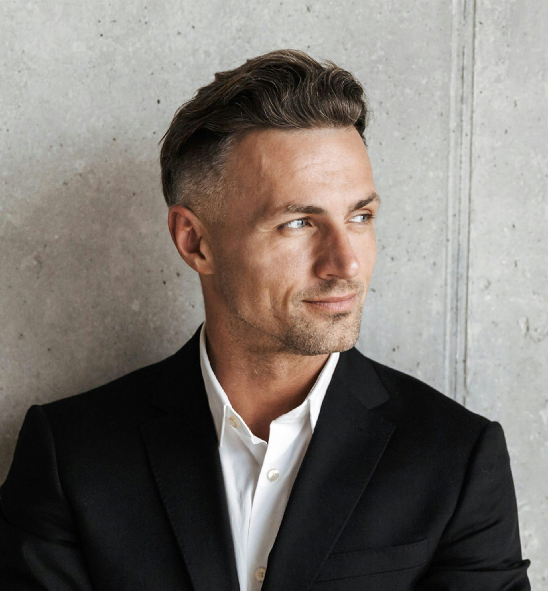 Man posing in front of concrete wall.