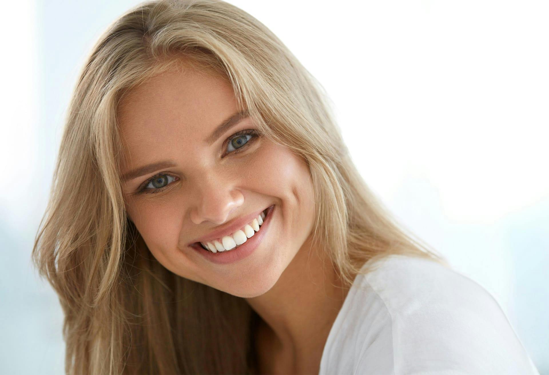 tan blonde model smiling at the camera in a white t-shirt